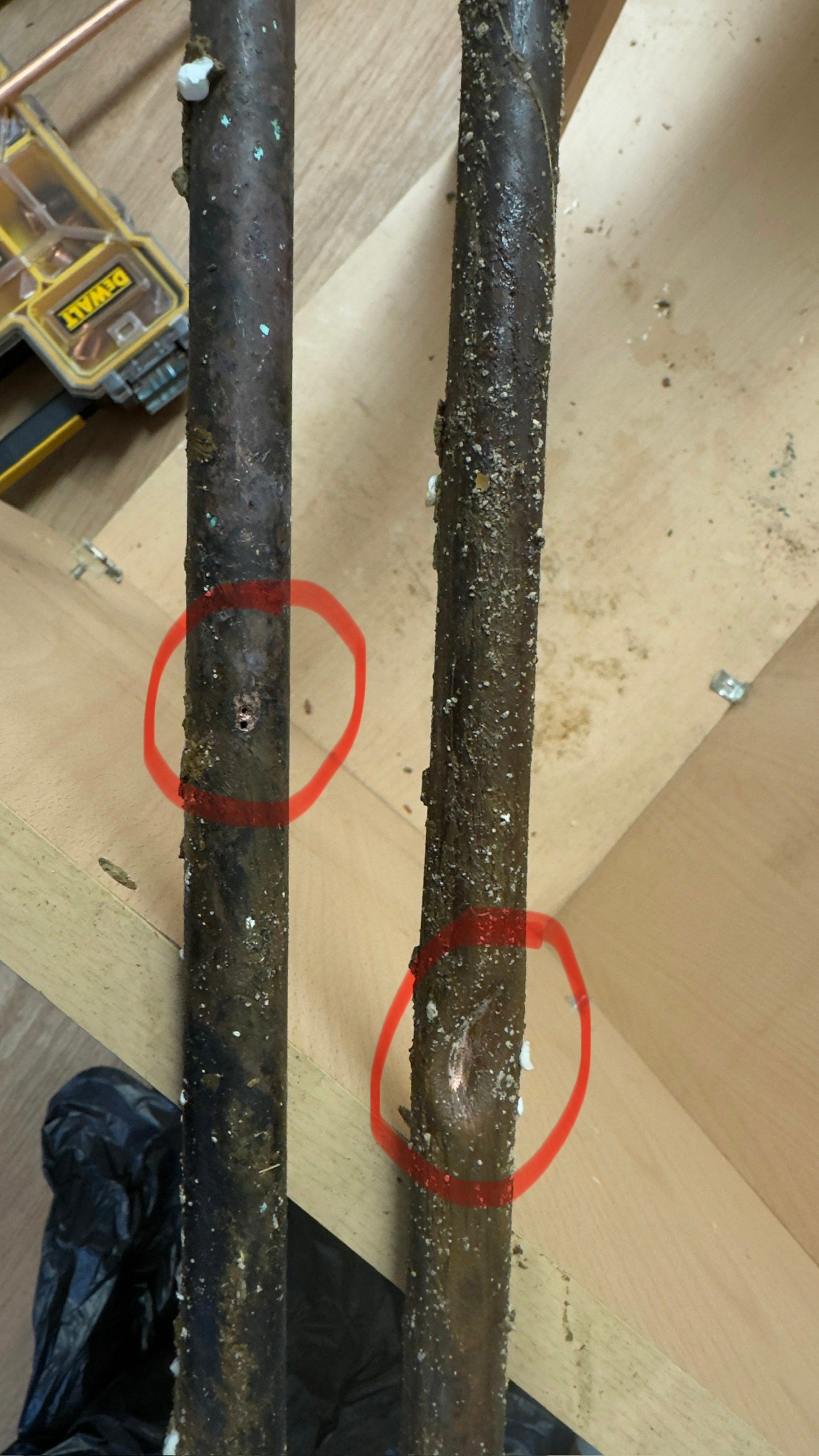 Removed corroded copper pipes showing pinhole leaks and future failure point circled in red