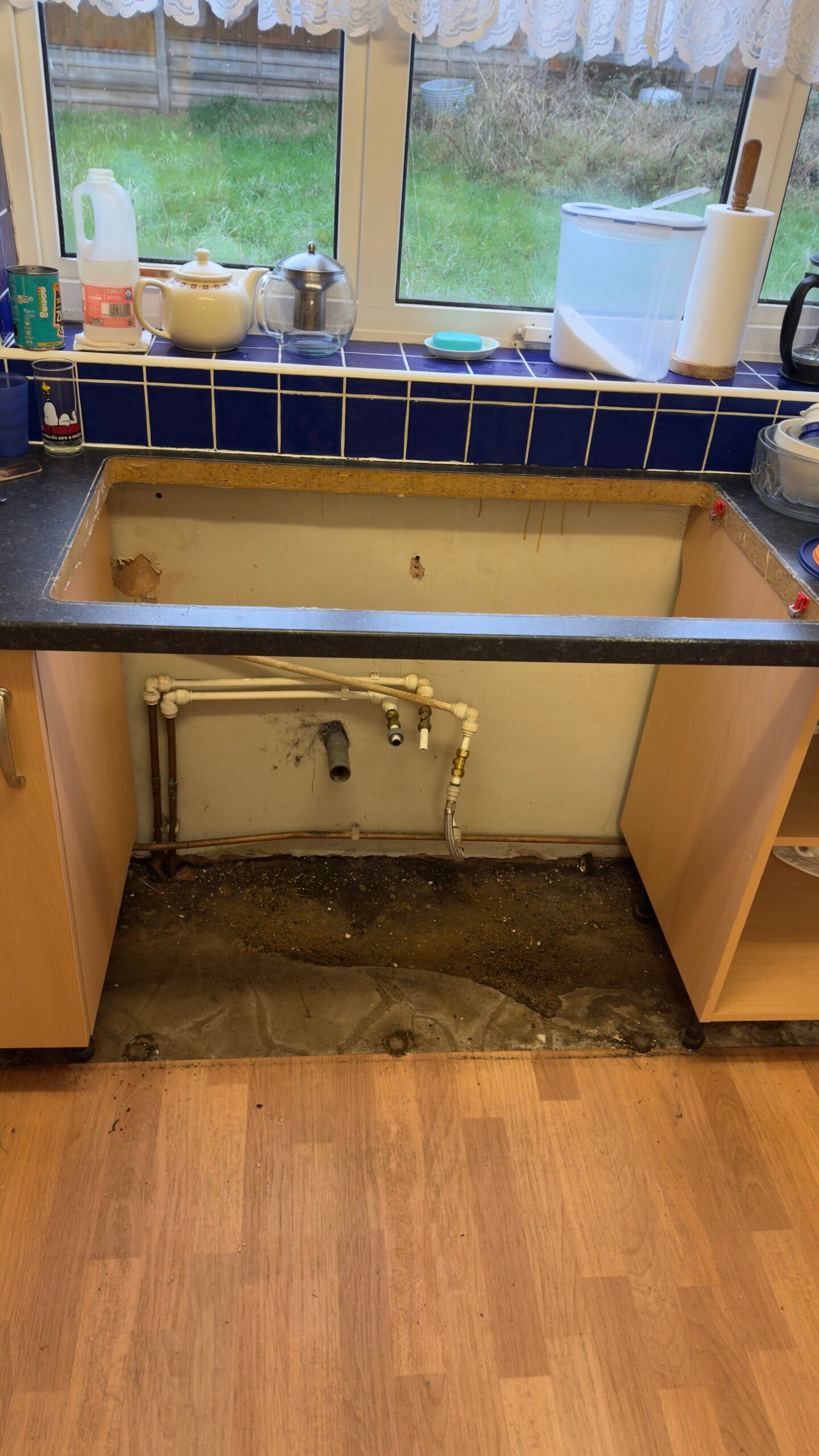 Kitchen cabinet removed — pipes and wet ground exposed underneath